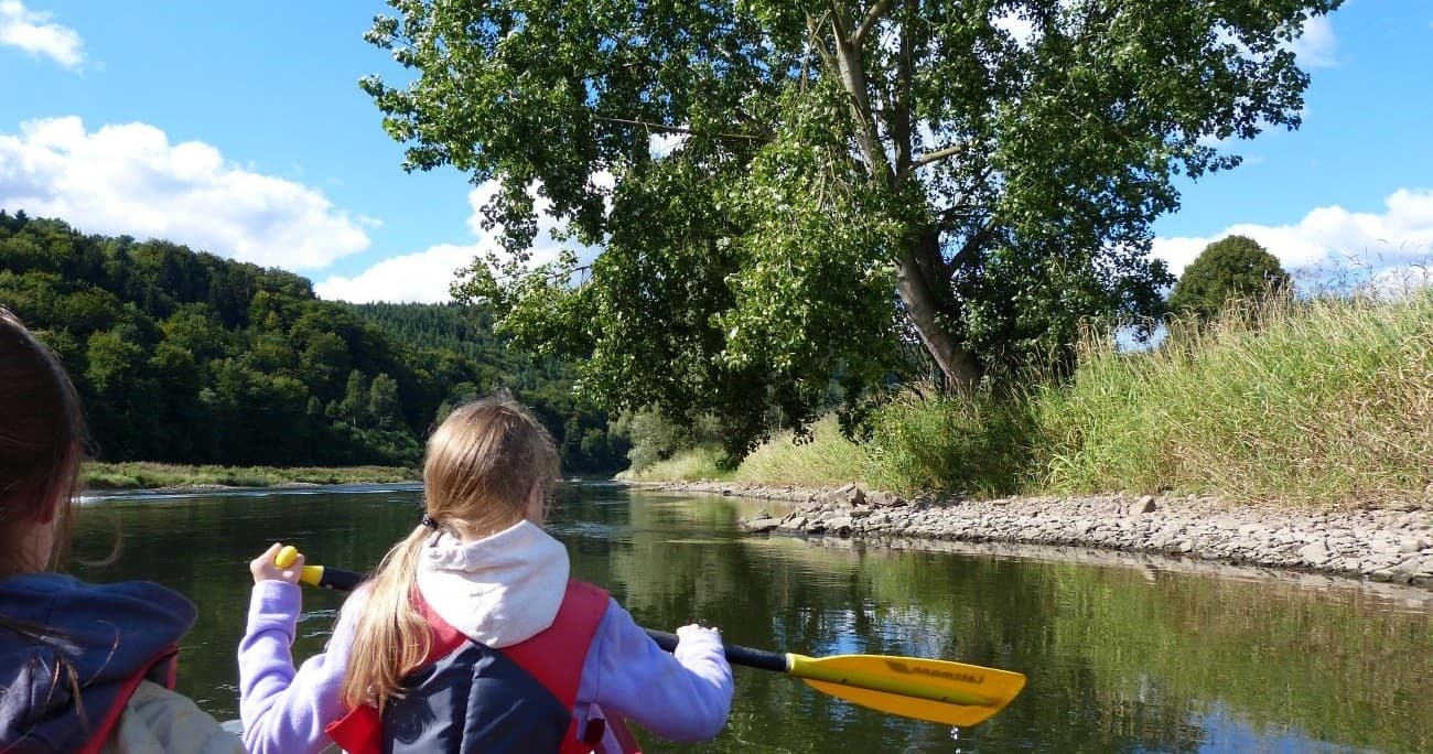 Children kayaking on calm river with grassy banks and trees