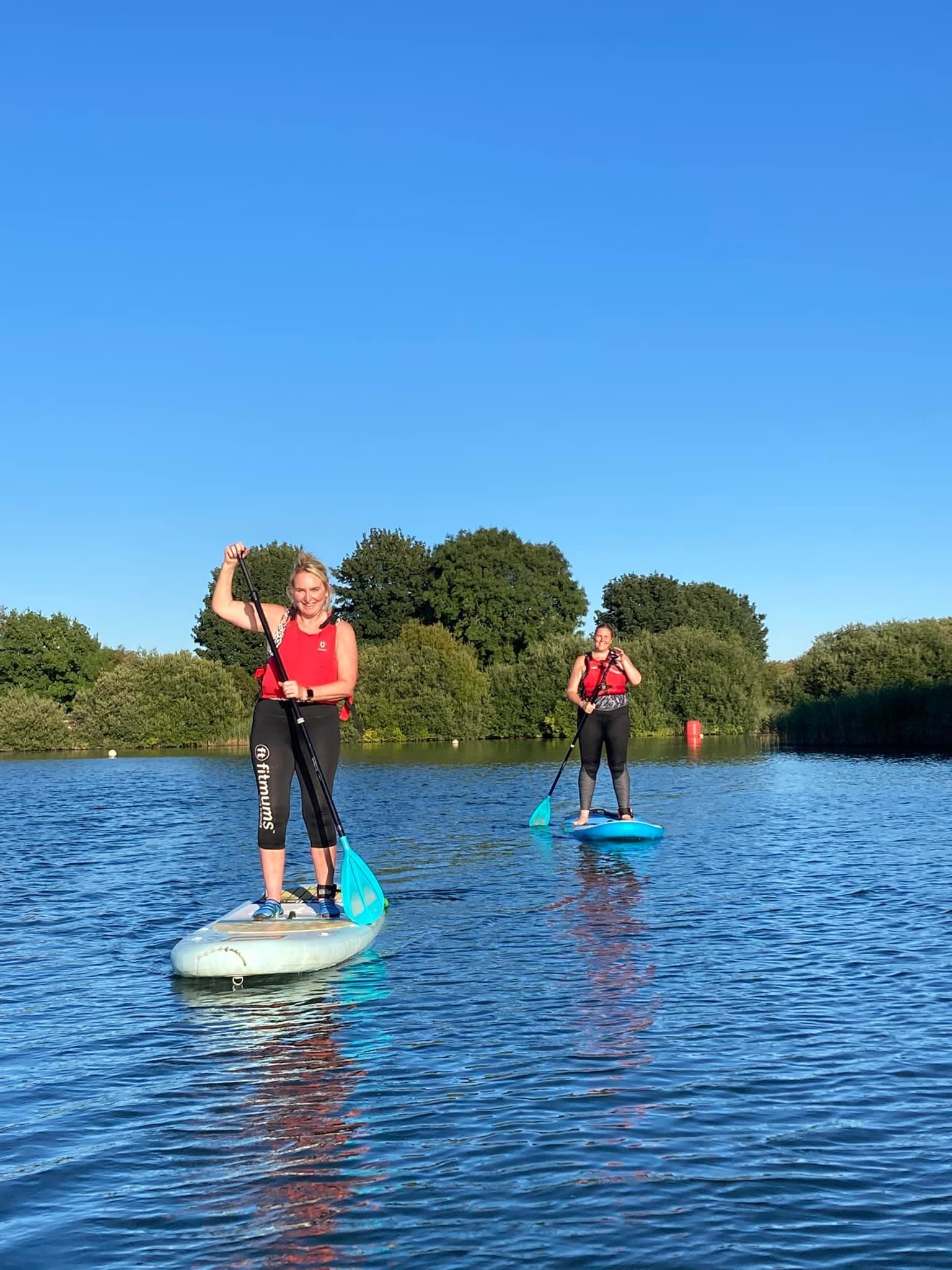 Two paddleboarders cruising on bright lake under clear blue sky