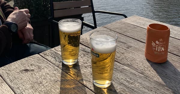Two pints on wooden table at waterfront beer patio enjoying riverside drinks