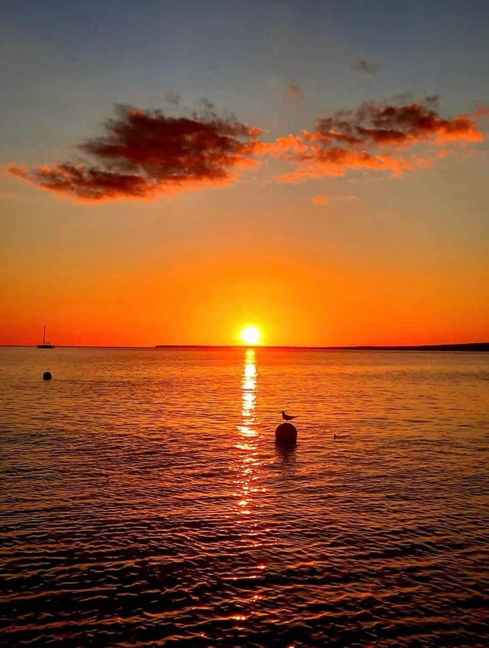 Sunset over open sea with silhouetted buoy and sailing horizon
