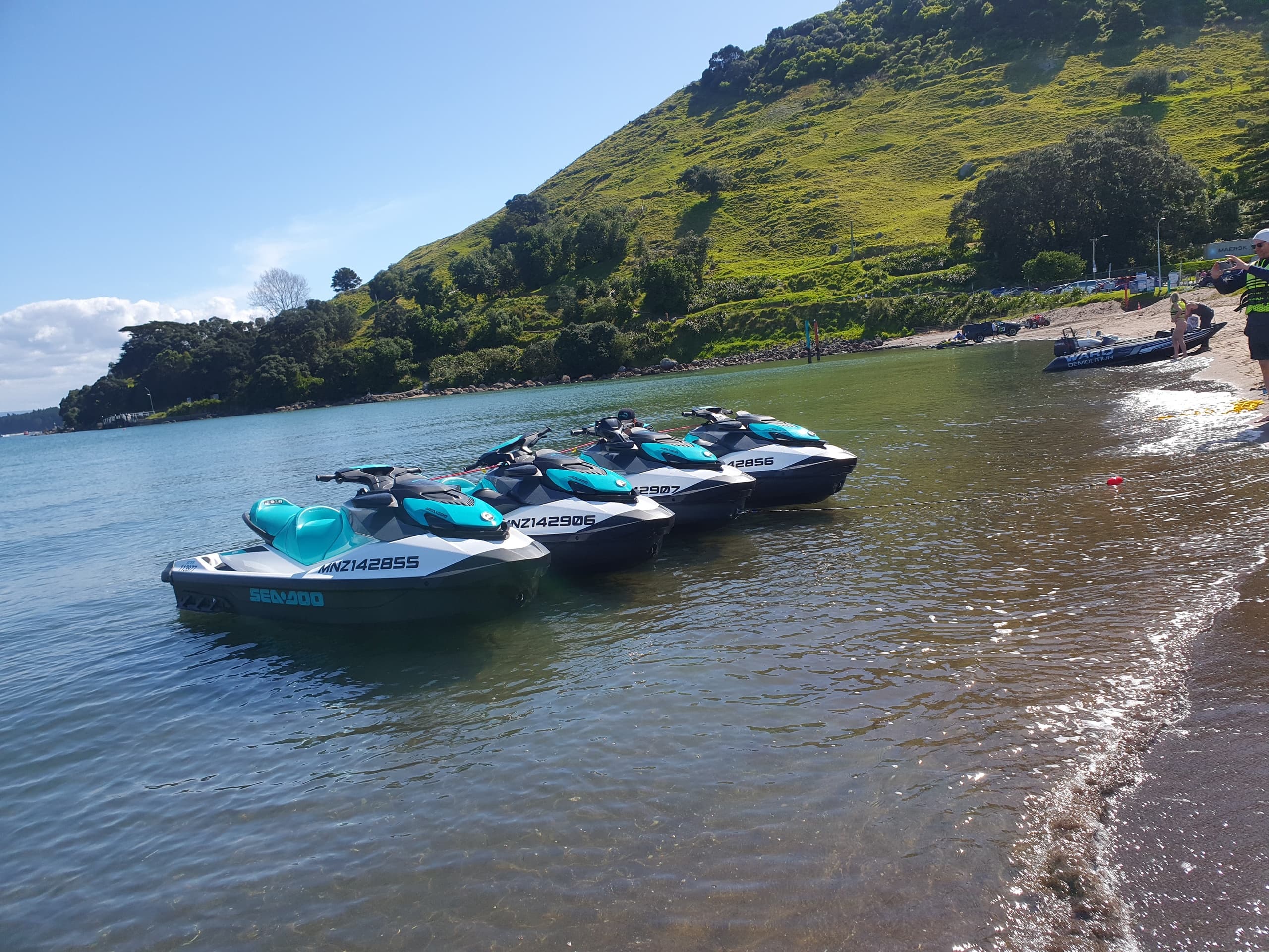Three jet skis beached in shallow water by green hillside