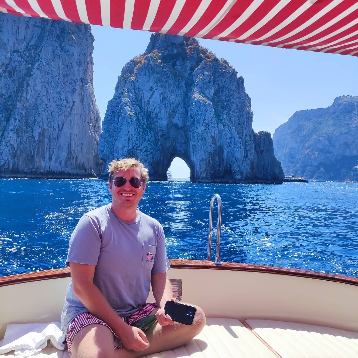 Smiling guest posing on boat with towering coastal rock arch backdrop