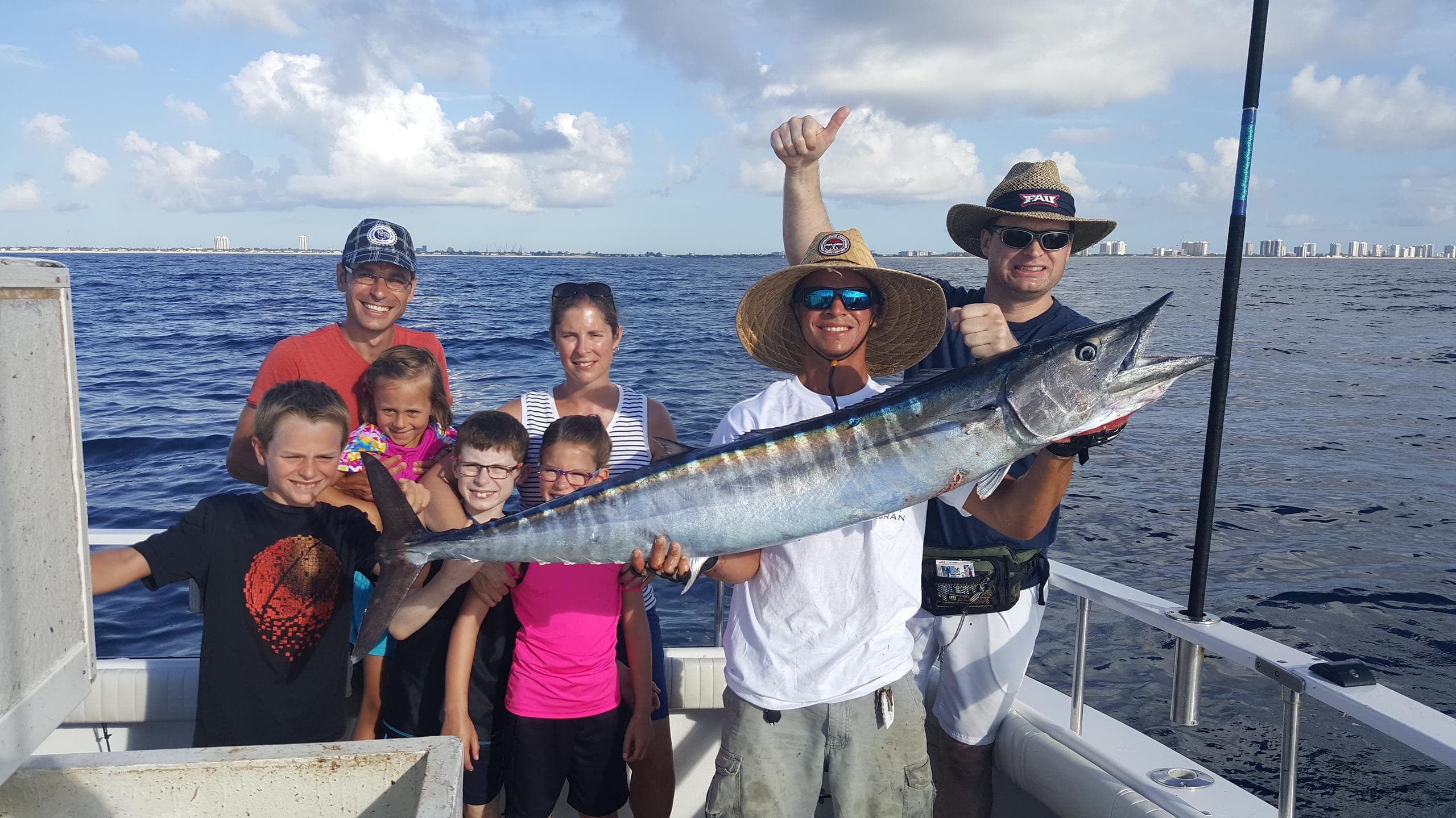 Family and crew holding large wahoo offshore during sportfishing charter
