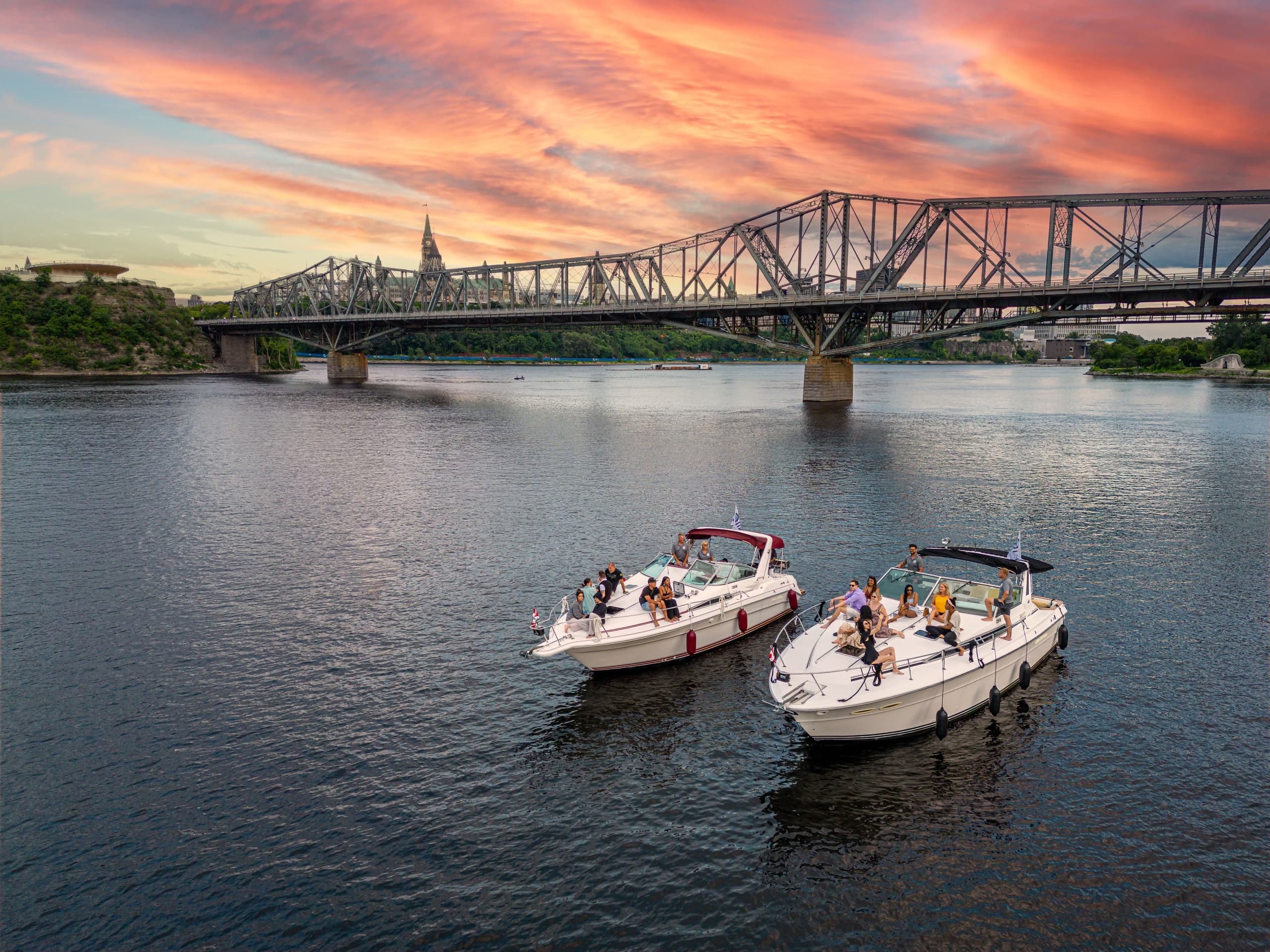 Two motorboats cruising near riverside bridge at sunset