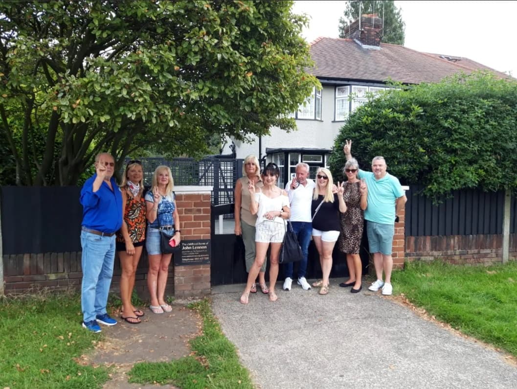 Small group touring Beatles home exterior on suburban driveway