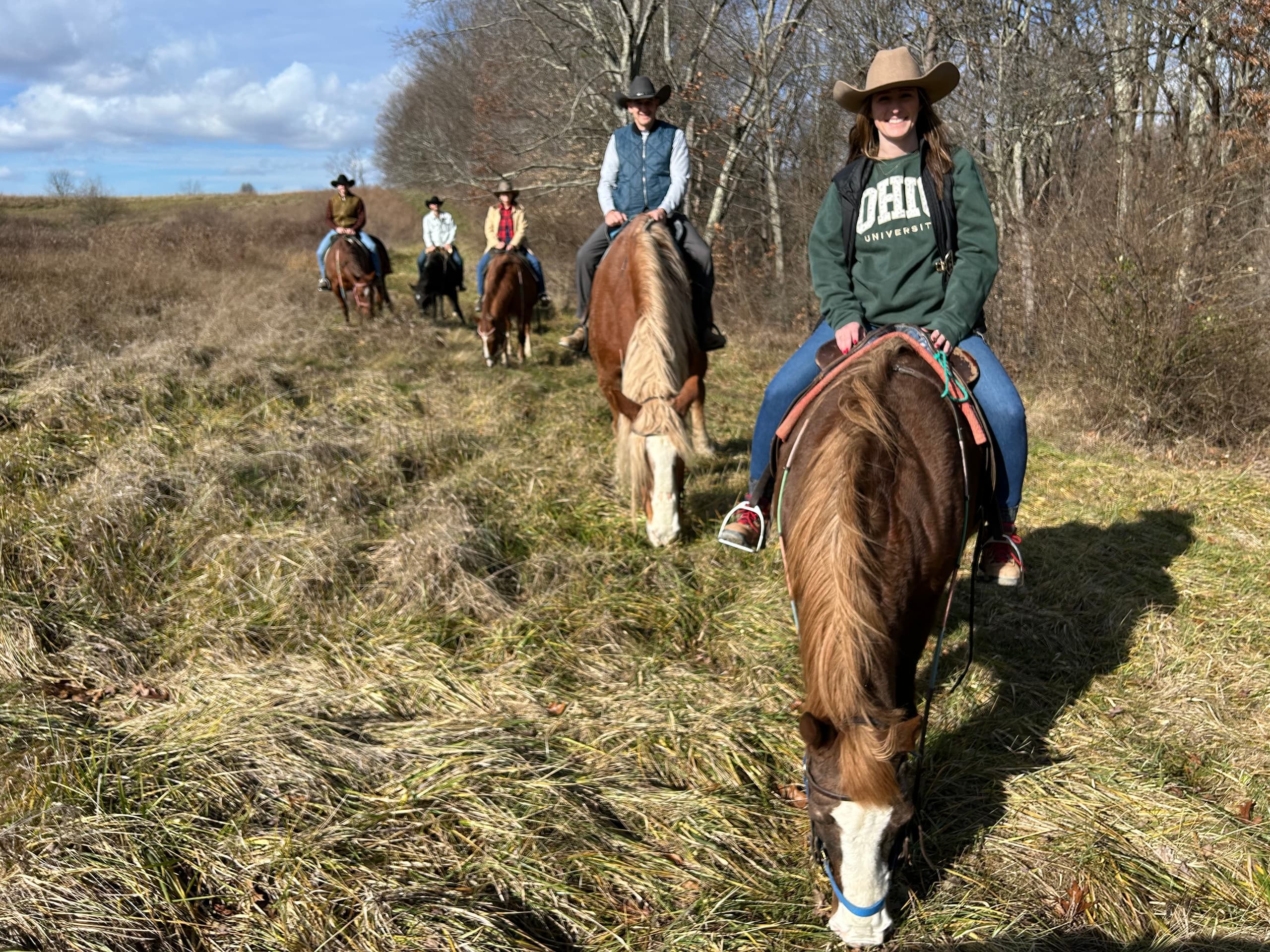 Line of riders trotting across open pasture at dusk