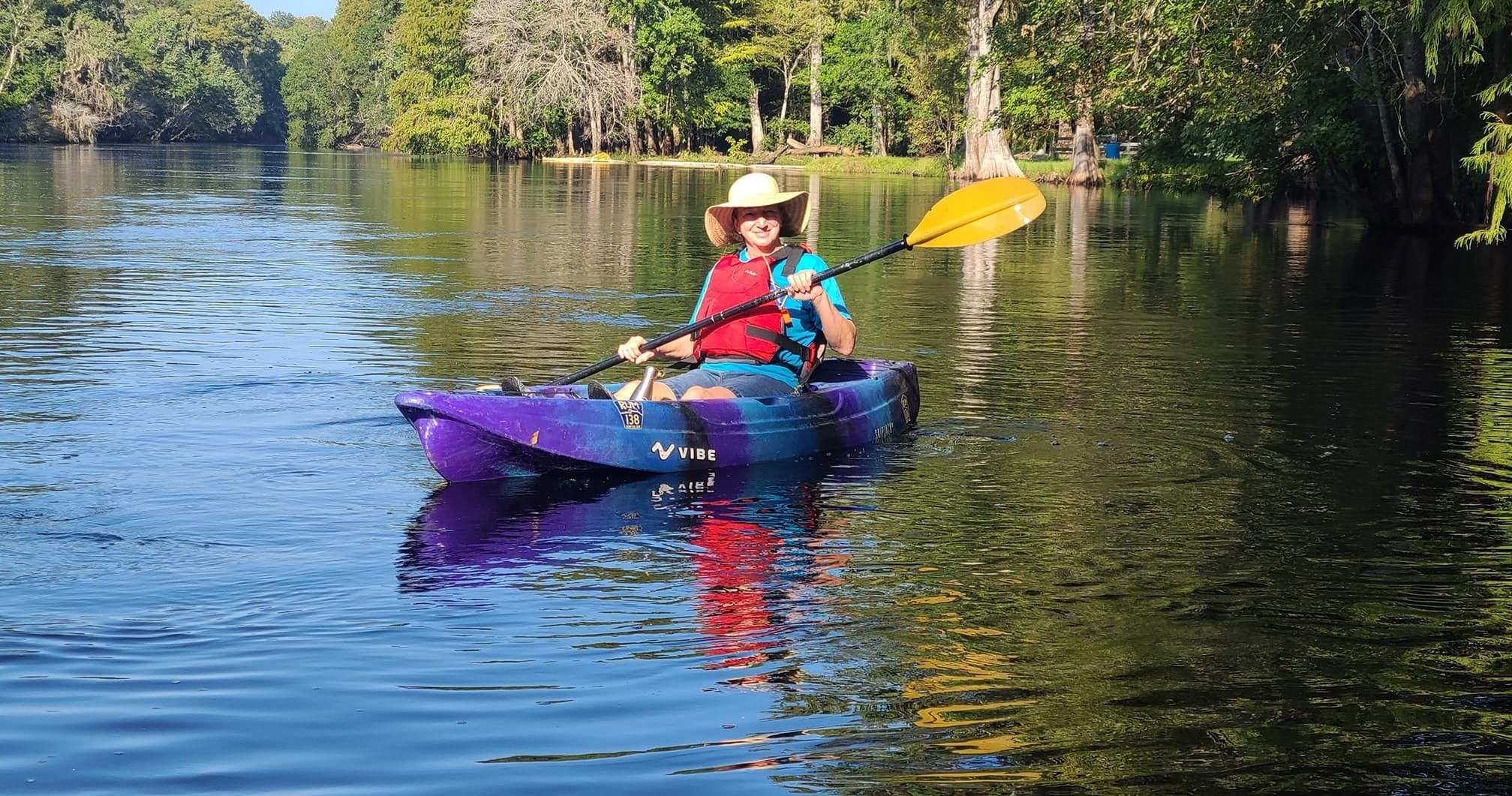 Solo kayaker paddling on calm, forest-lined river at midday