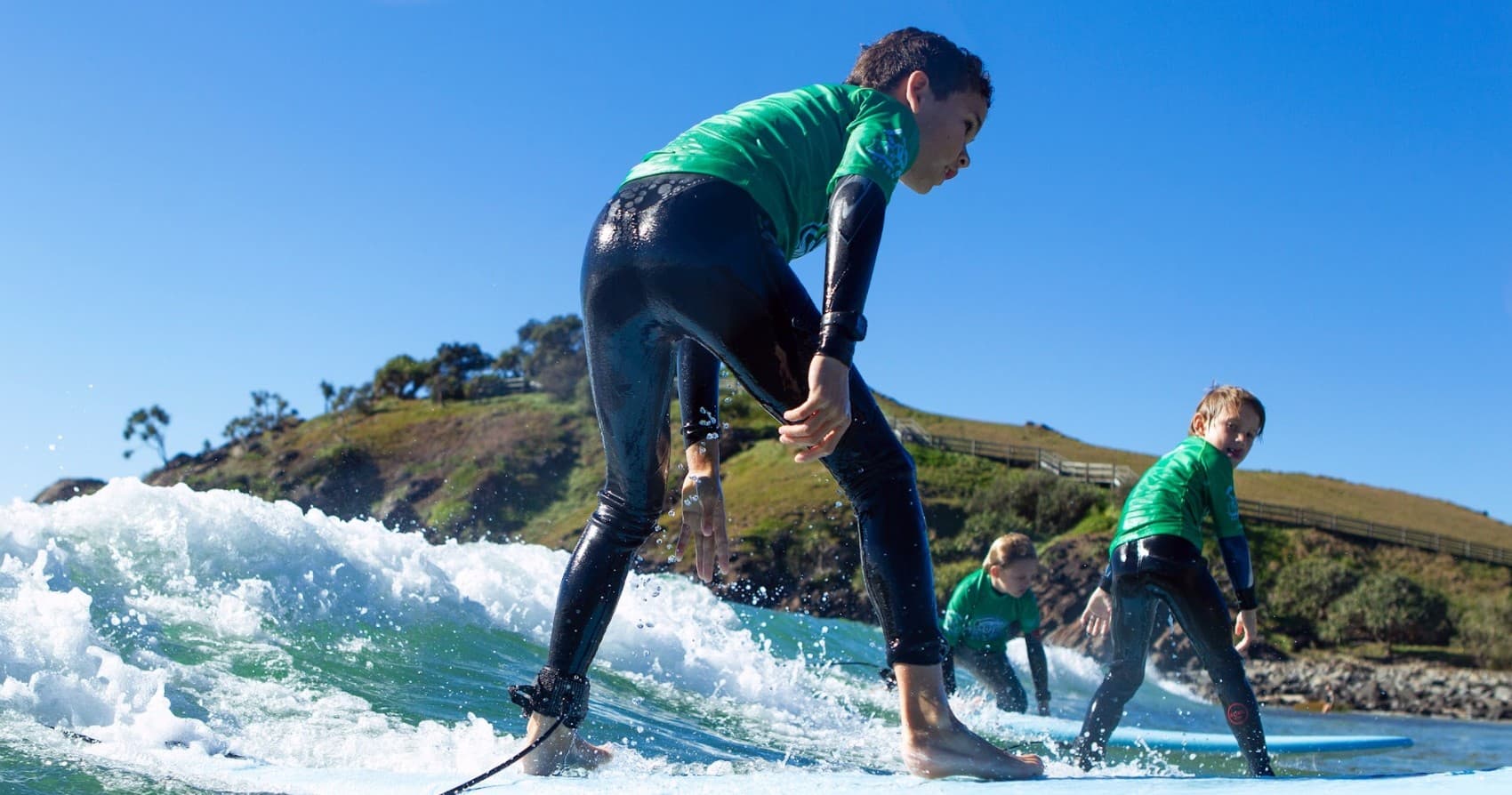 Surfers balancing on waves with coastal hills in background