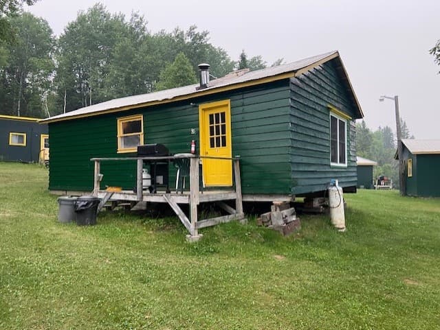 Raised green cabin with deck near wooded lakefront, rustic camping base