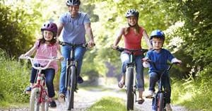 Family cycling together on sunny park trail with trees