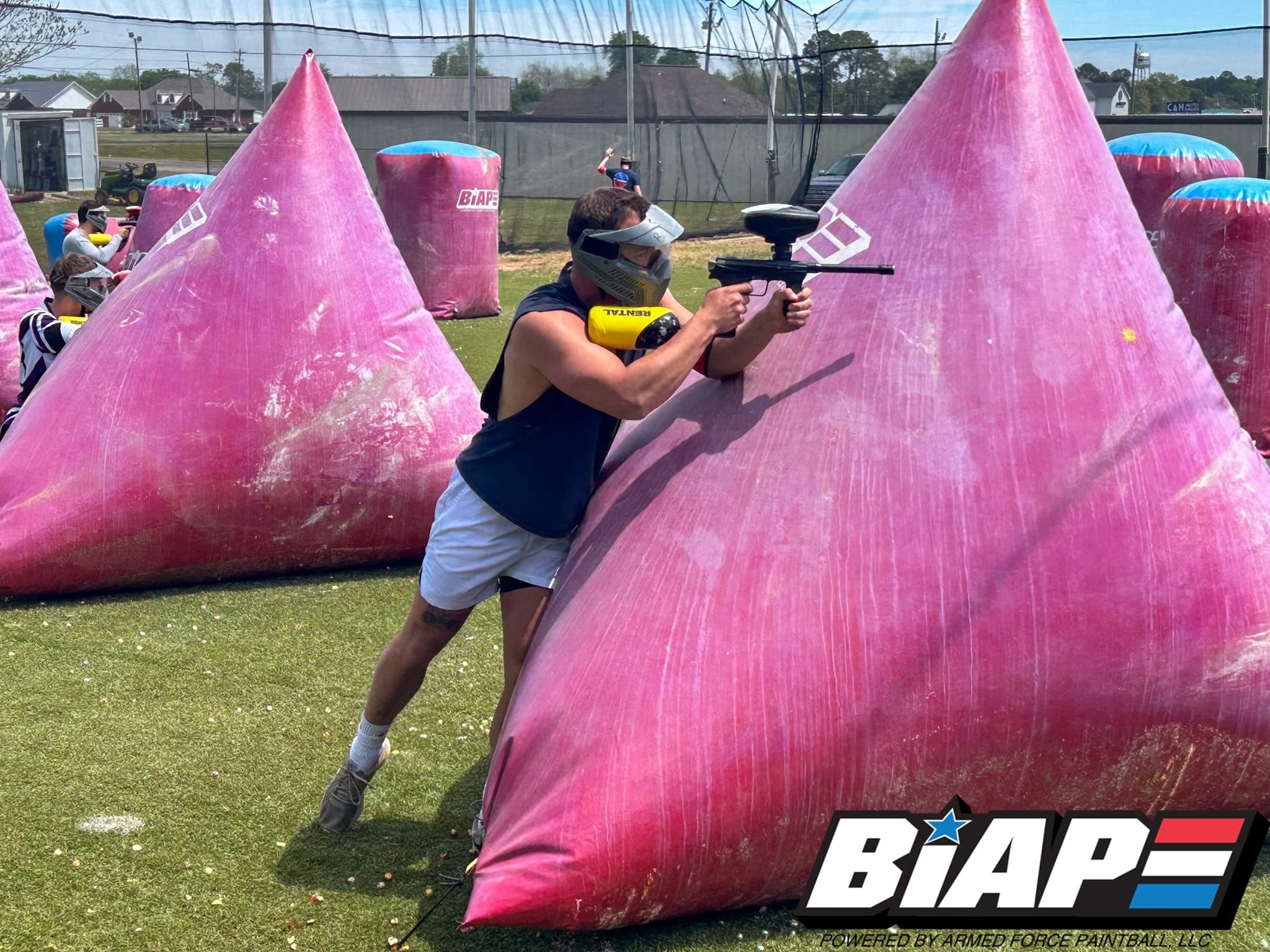Paintball player firing behind pink inflatable bunker on field