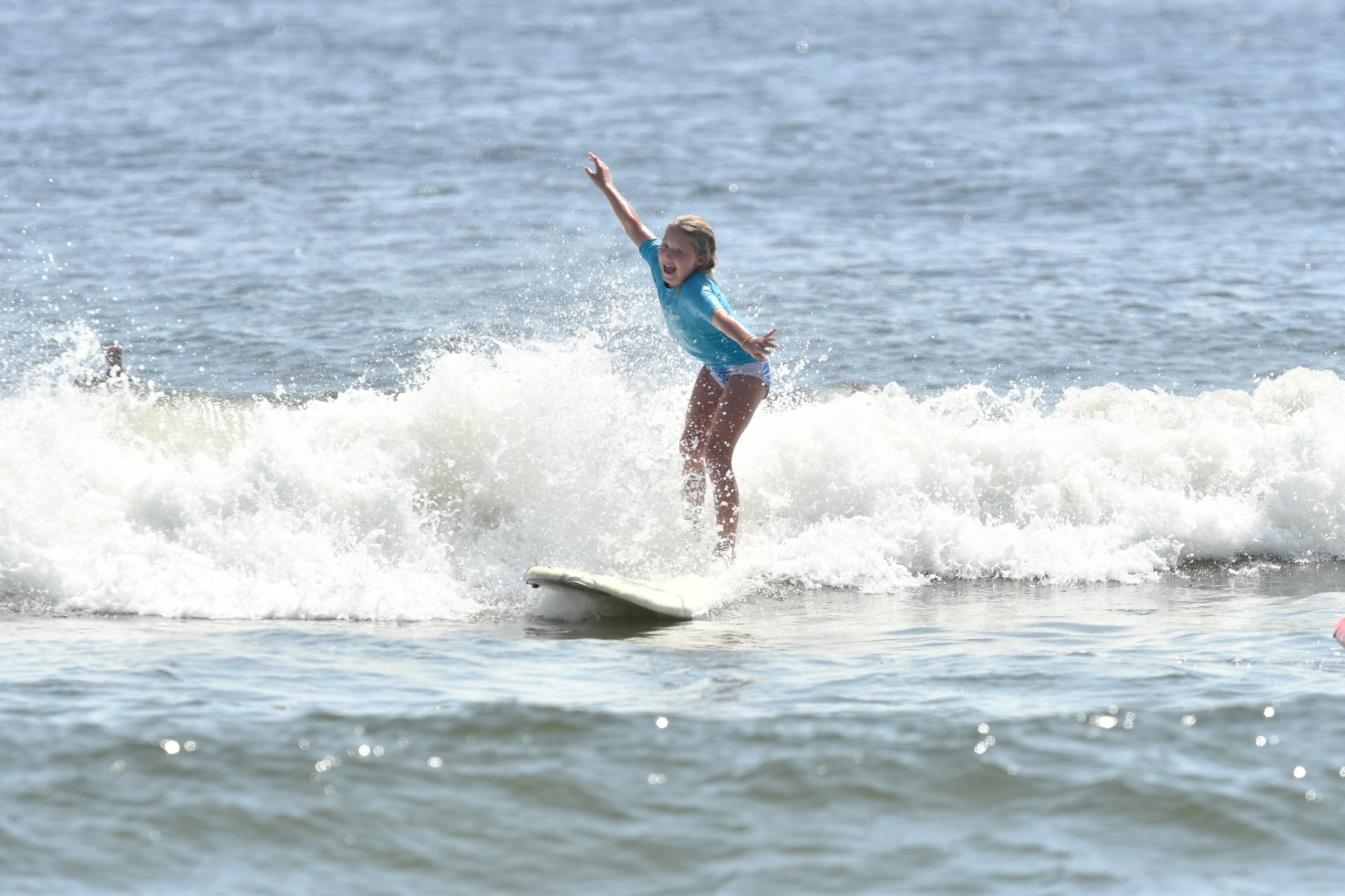 Stand-up surfer riding small breaking wave near sandy beach