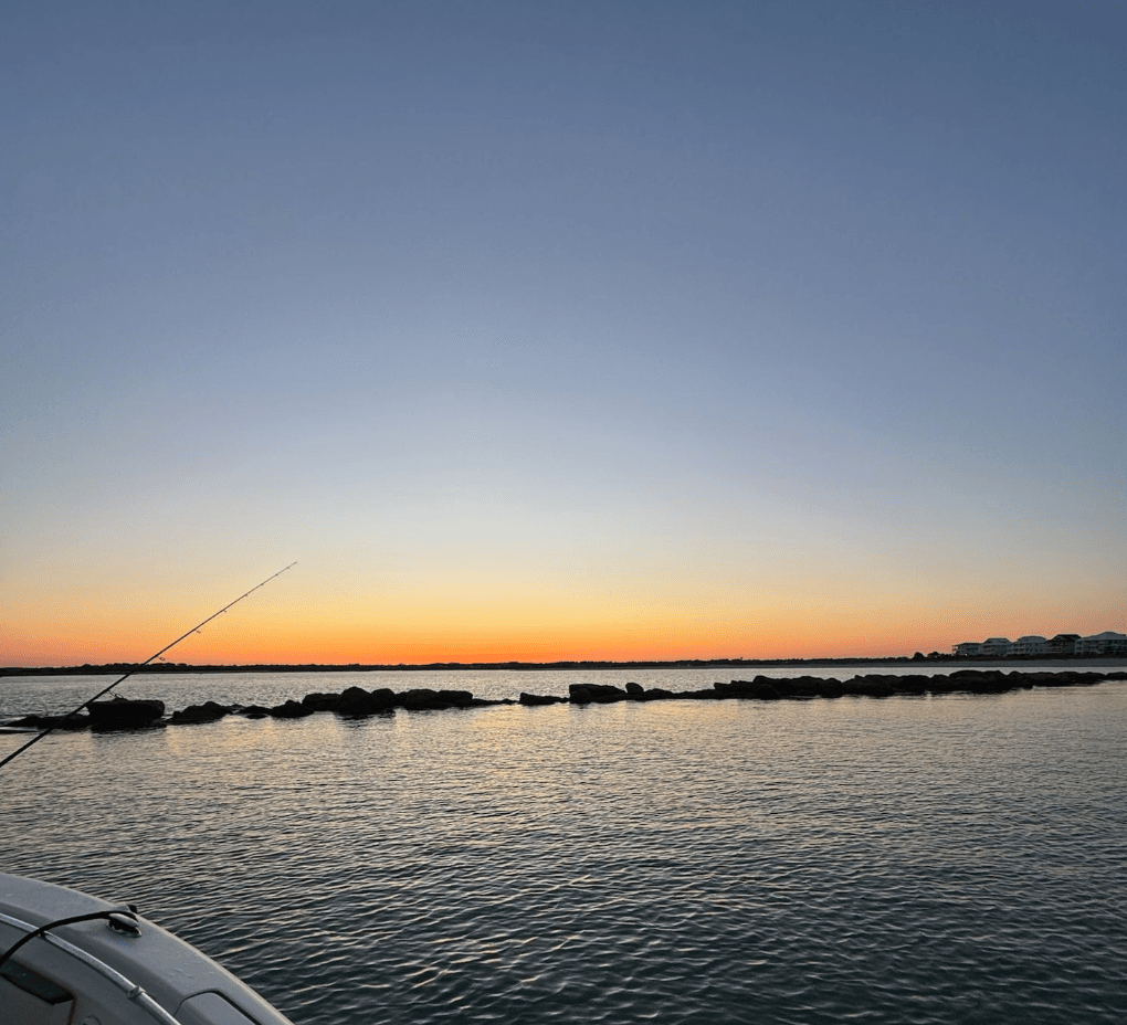 Calm sunrise over inlet with fishing rod and boat deck in foreground