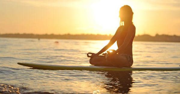 Paddleboarder meditating at sunset on calm coastal waters