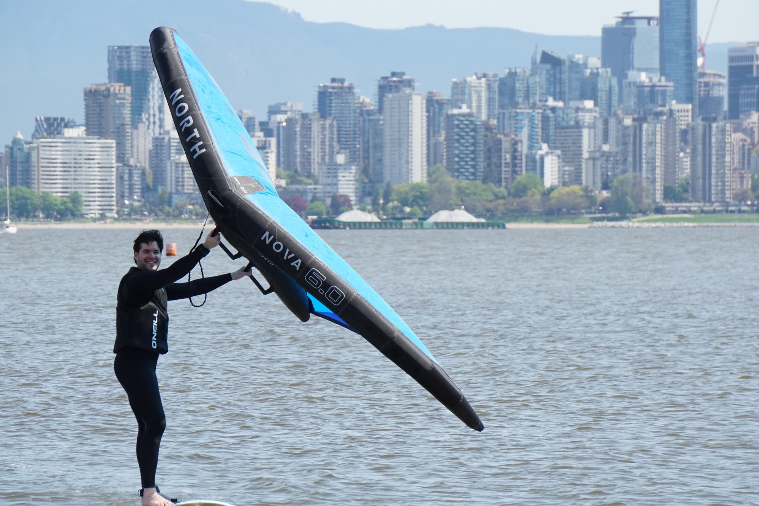 Person carrying wingboard on beach with city skyline