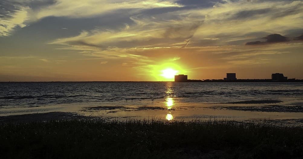 Sunset over ocean shoreline with calm water and silhouetted skyline