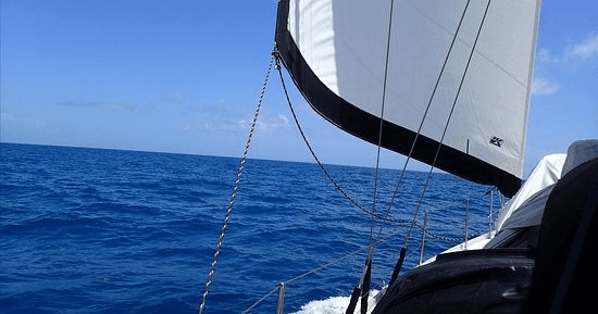 Sailboat cruising on open blue ocean with full white sail