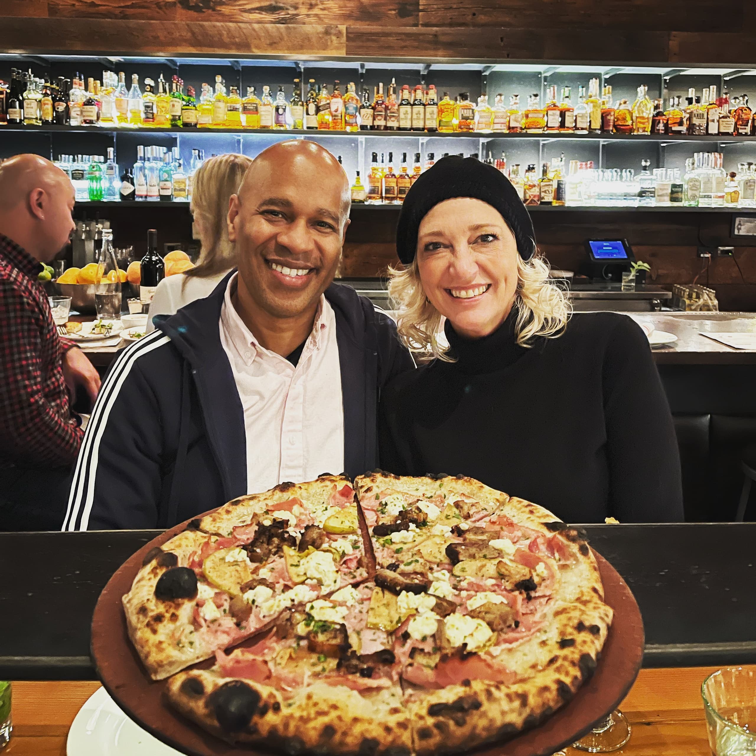 Couple smiling with pizza at cozy Portland bar, food tour