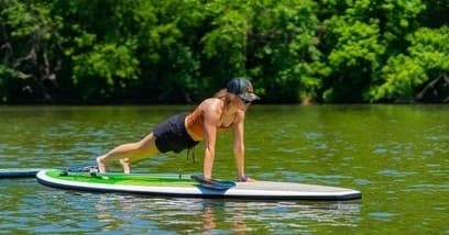Woman practicing SUP yoga on paddleboard near wooded shore