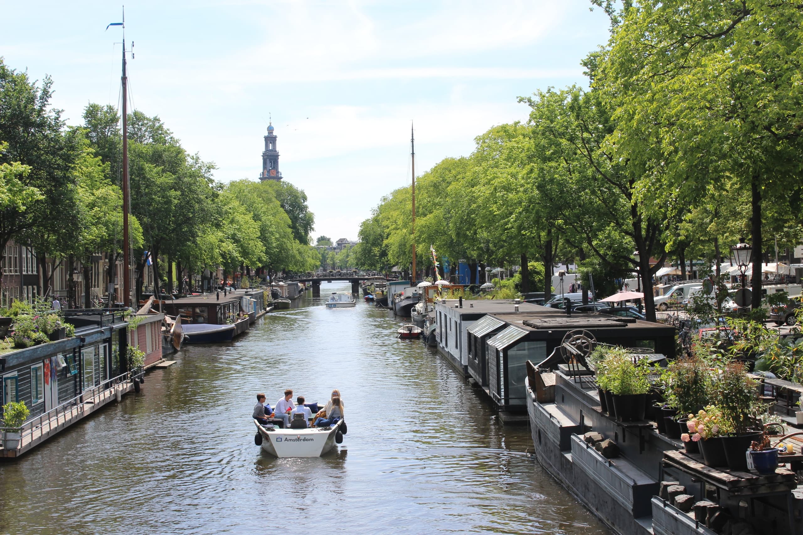 Small boat gliding through green, tree-lined Amsterdam canal