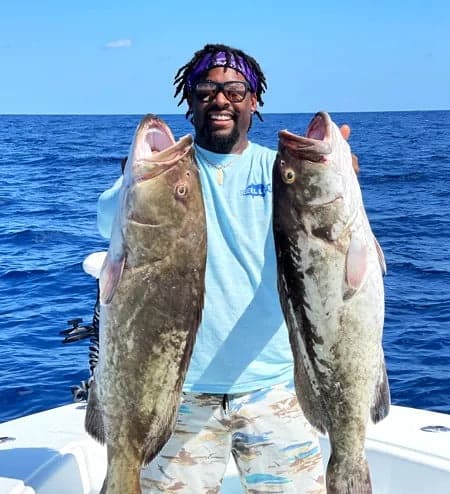 Fisherman holding two large offshore grouper on blue ocean