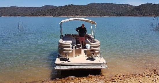 Pontoon boat beached on clear lake shore with wooded hills