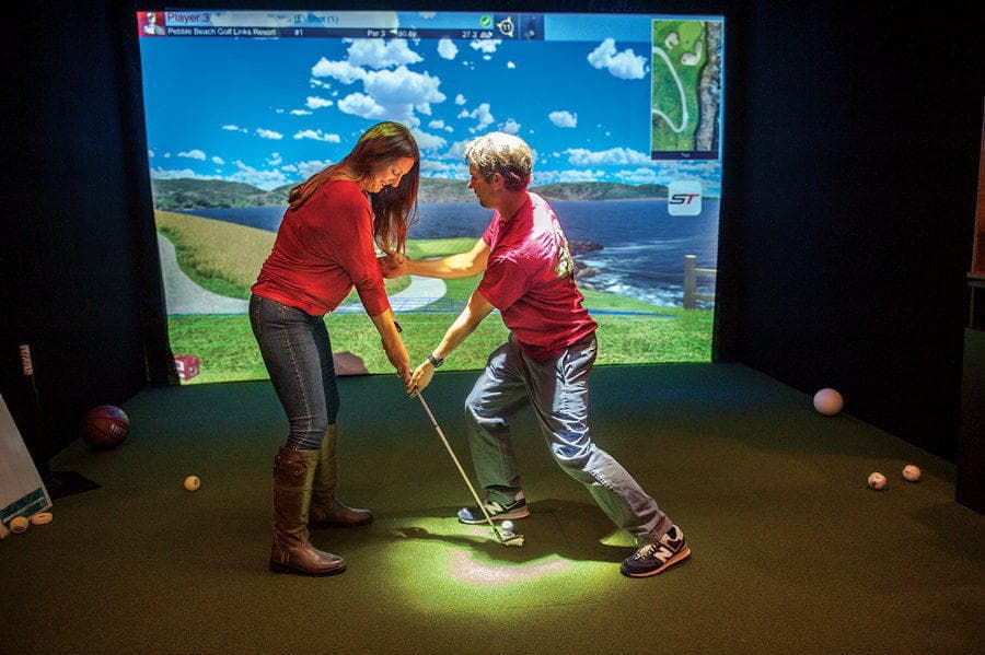 Instructor coaching student in indoor golf simulator lesson