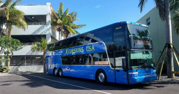 Double-decker tour bus parked by palm trees for island excursions