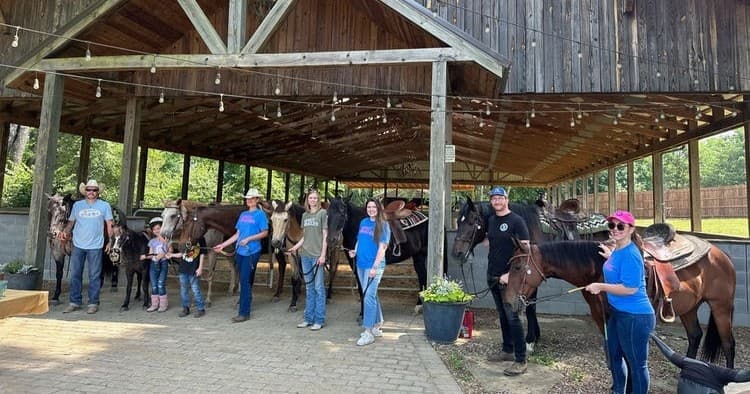 Group horseback riders preparing at rustic barn stables outdoors