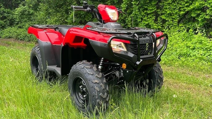 Red all-terrain ATV parked in grassy field near woods