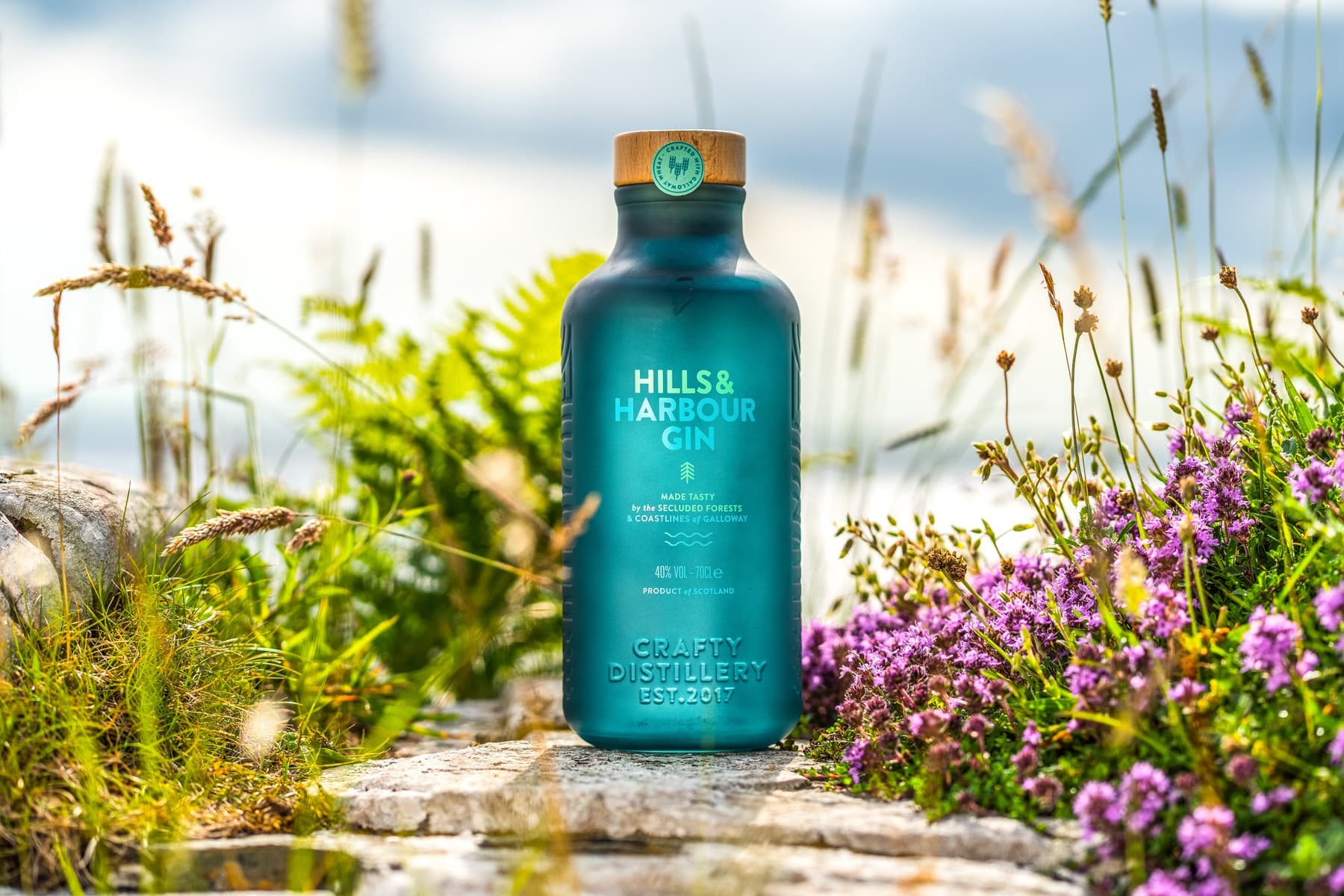 Gin bottle on coastal rocks with wildflowers, seaside tasting
