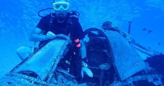 Diver exploring sunken wreck on blue seafloor in Hawaii waters