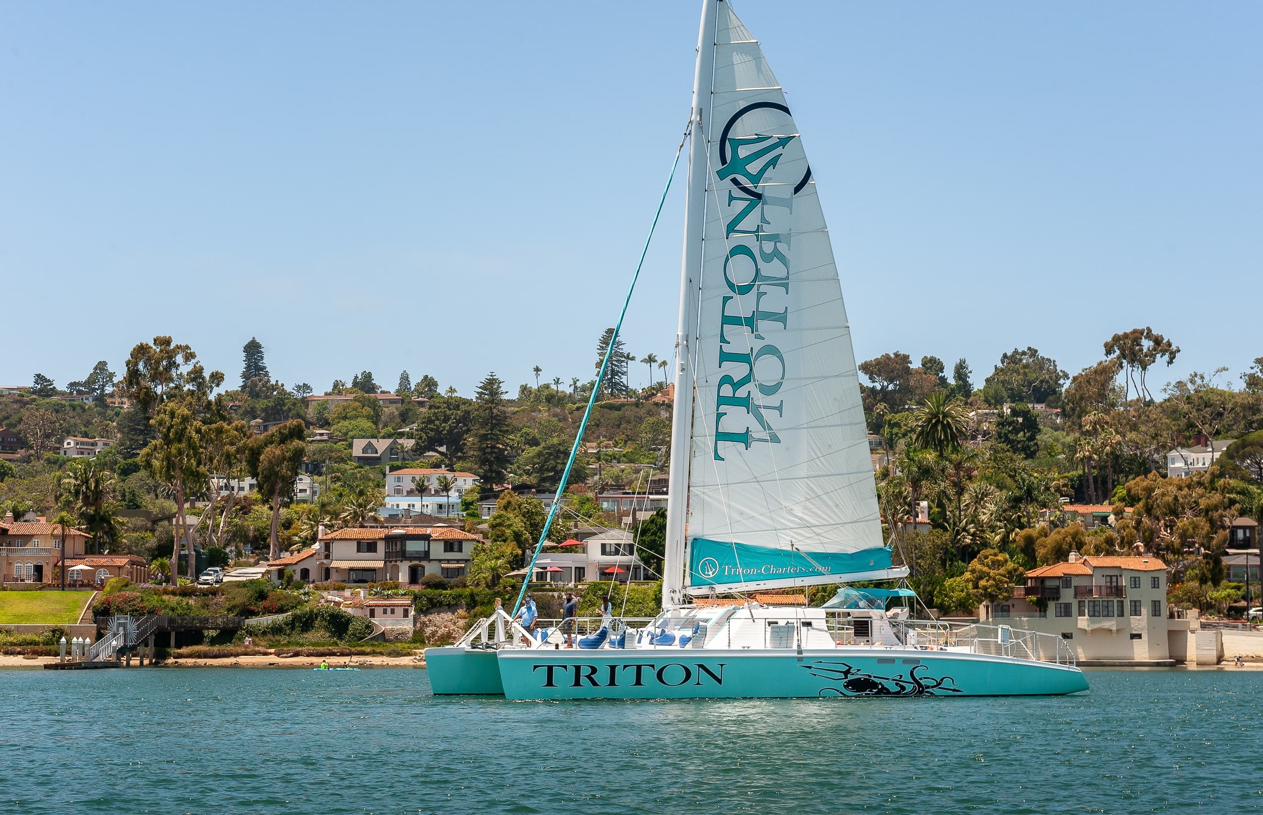 Triton catamaran sailing along coastal neighborhood, daytime cruise