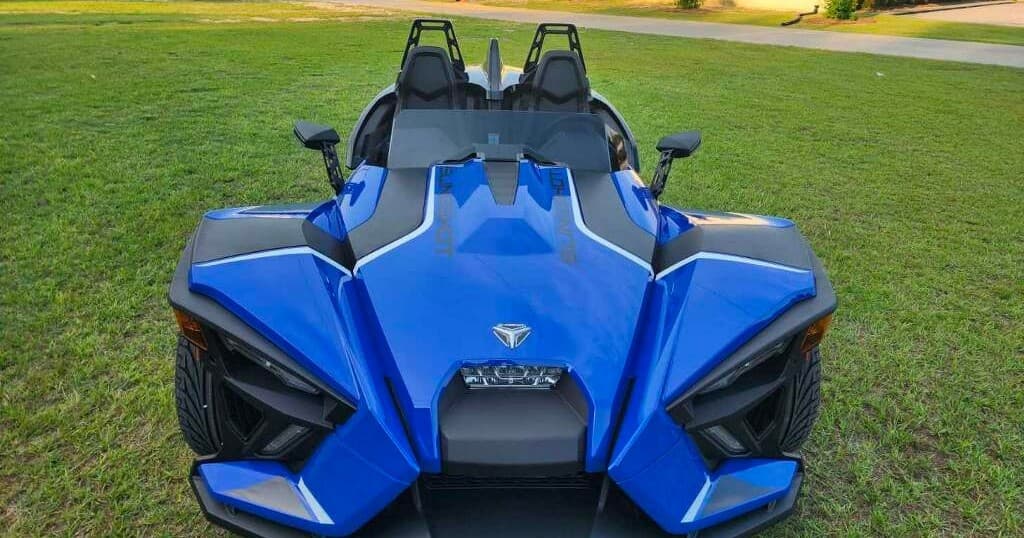 Blue Polaris Slingshot front view on grassy roadside