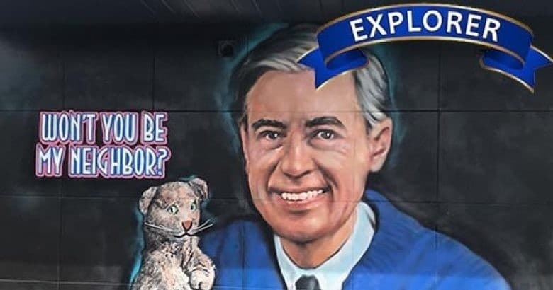 Colorful street mural of Mr. Rogers with 'Explorer' banner on wall