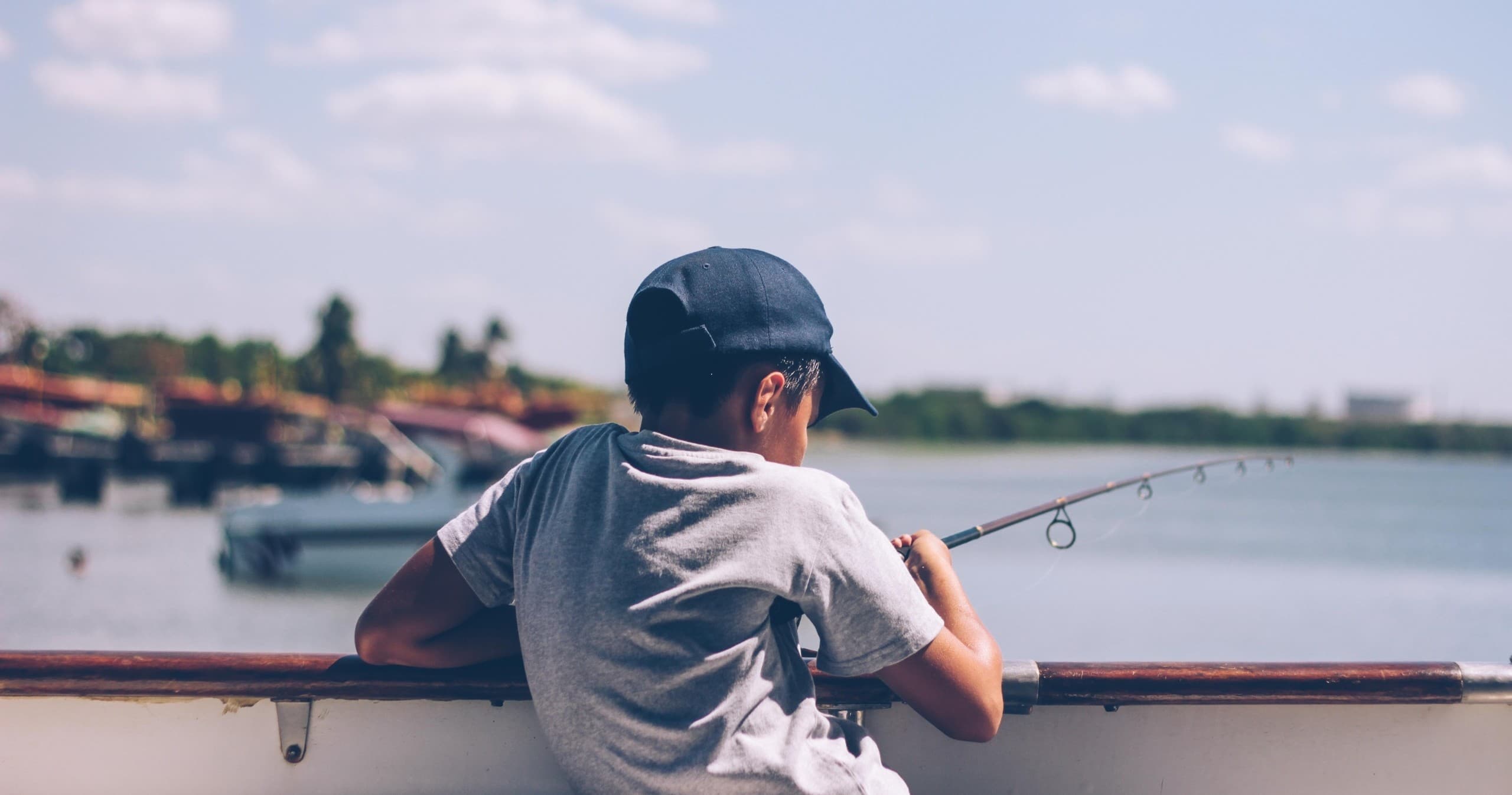 Child fishing from boat on calm harbor, family fishing trip