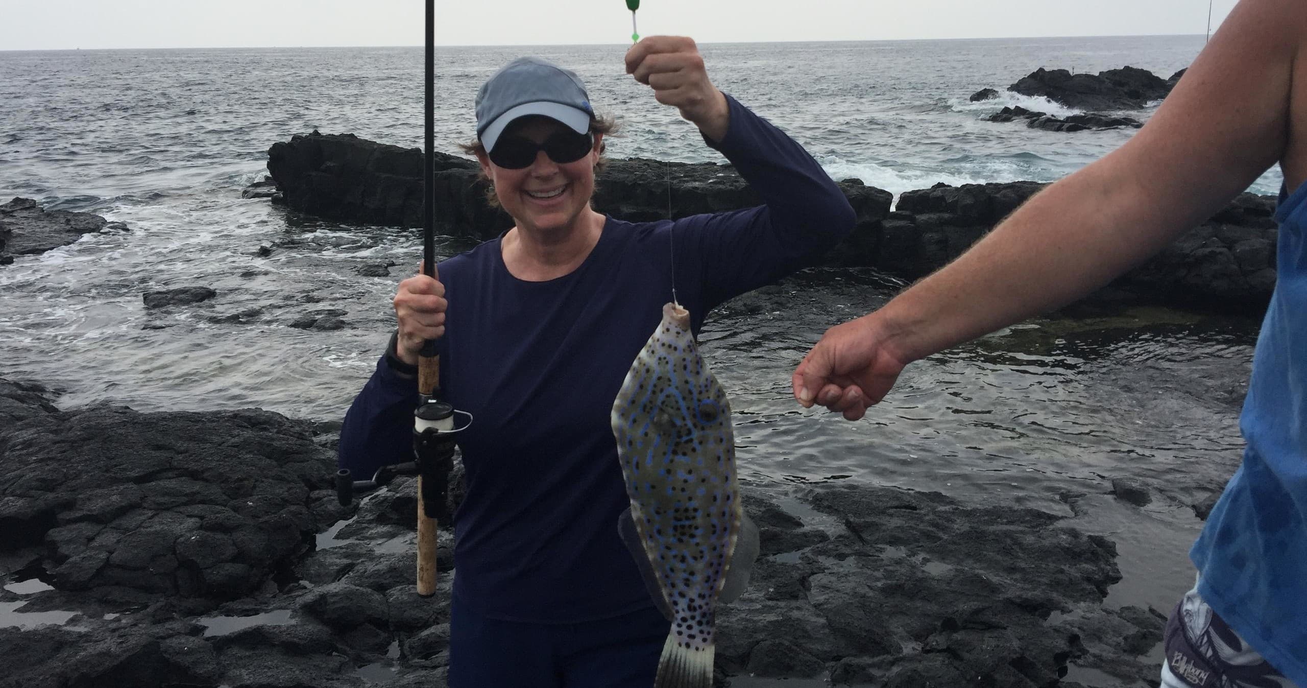 Angler holding caught fish on rocky ocean shore during fishing trip