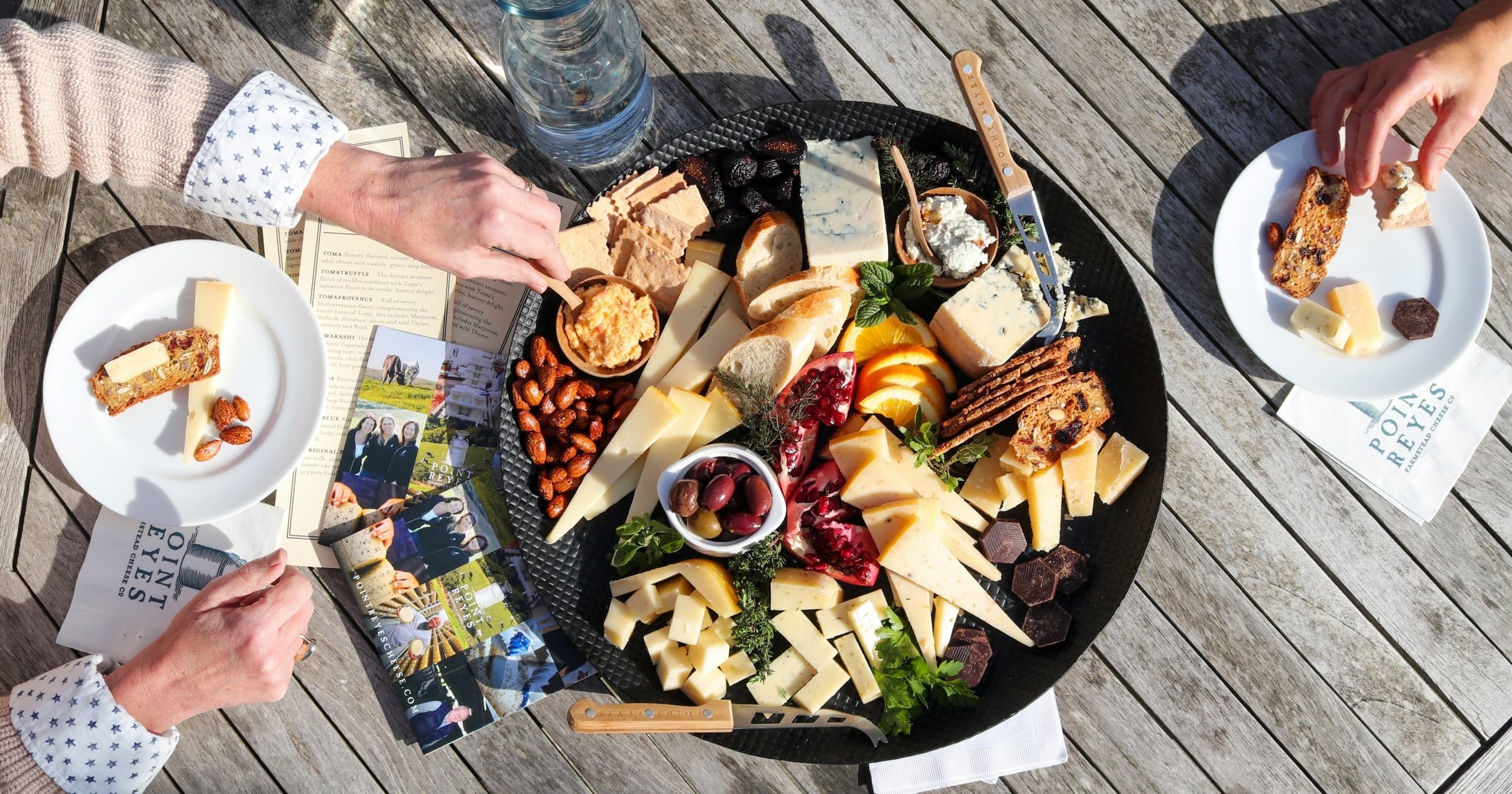 Outdoor cheese platter on wooden deck with friends sharing