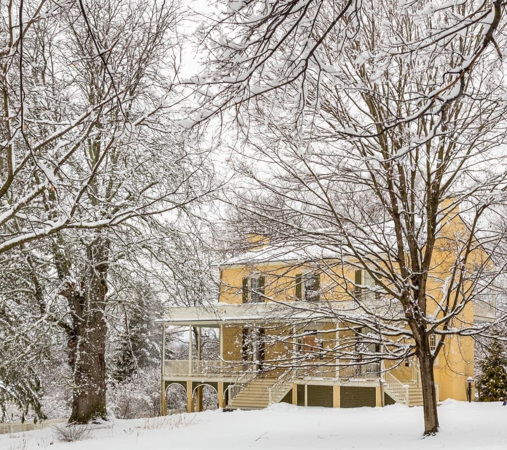 Snow-covered historic house and bare trees on winter estate grounds