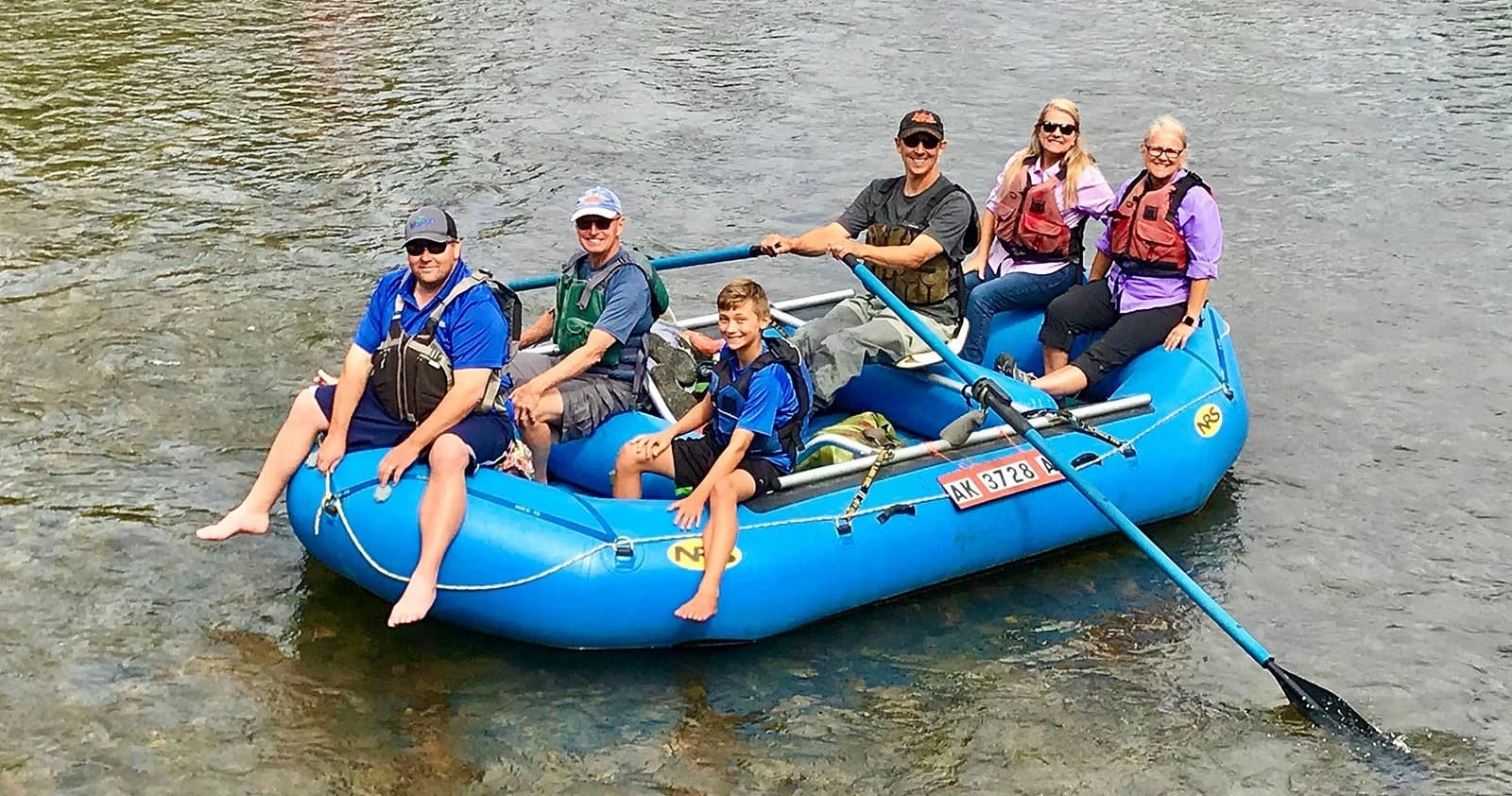 Family group rafting in shallow river, relaxed wilderness float trip