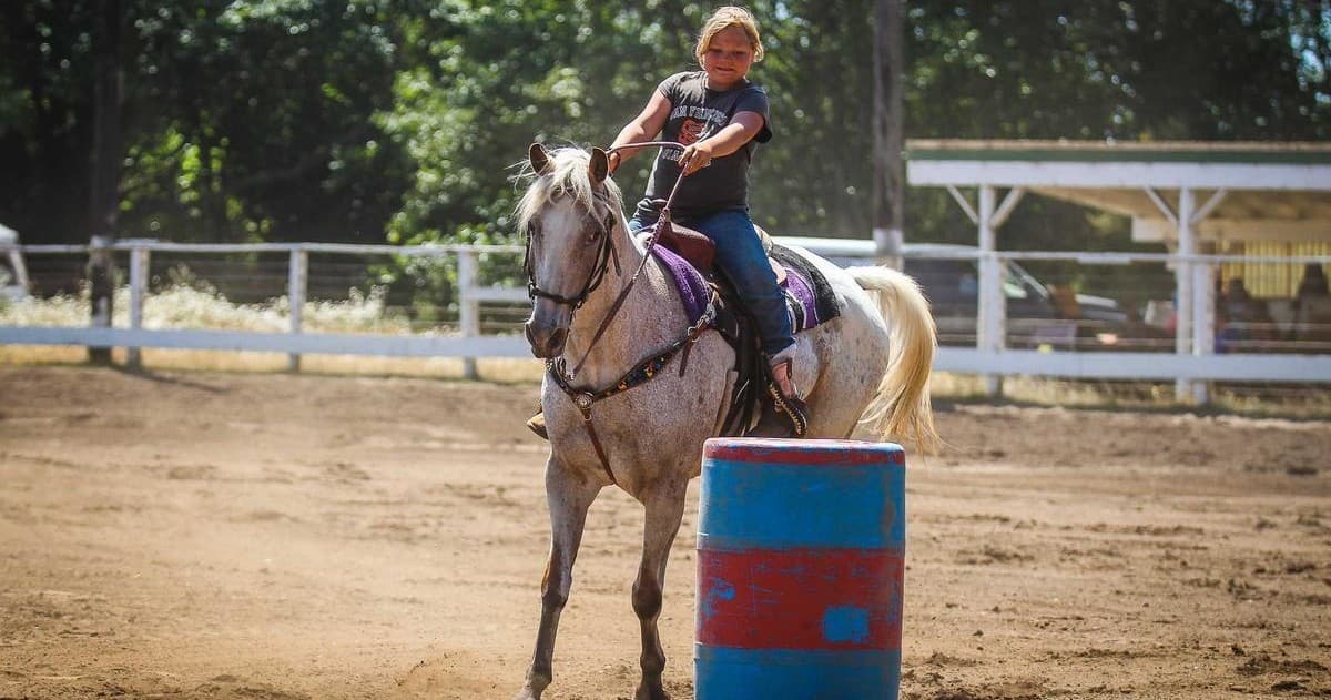 Youth barrel racing on galloping horse in dusty rodeo arena