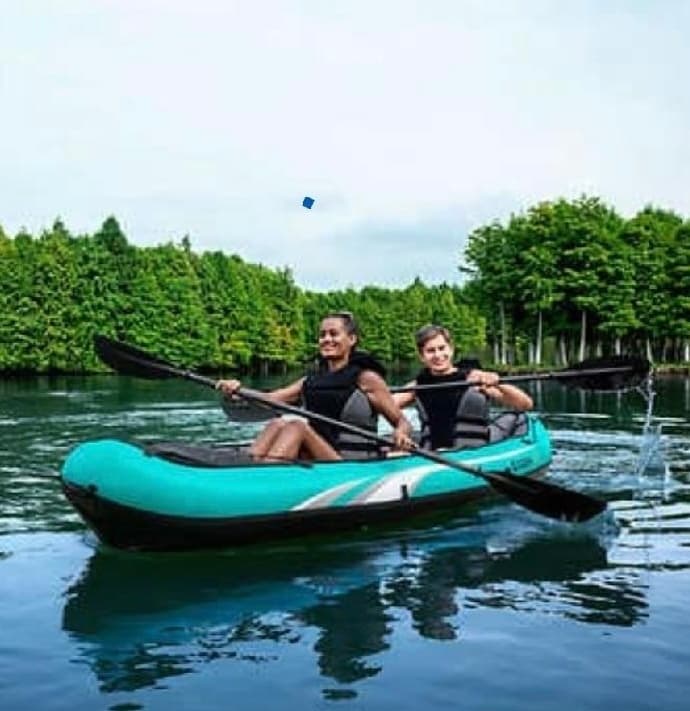 Two people paddling inflatable kayak on serene lake near trees