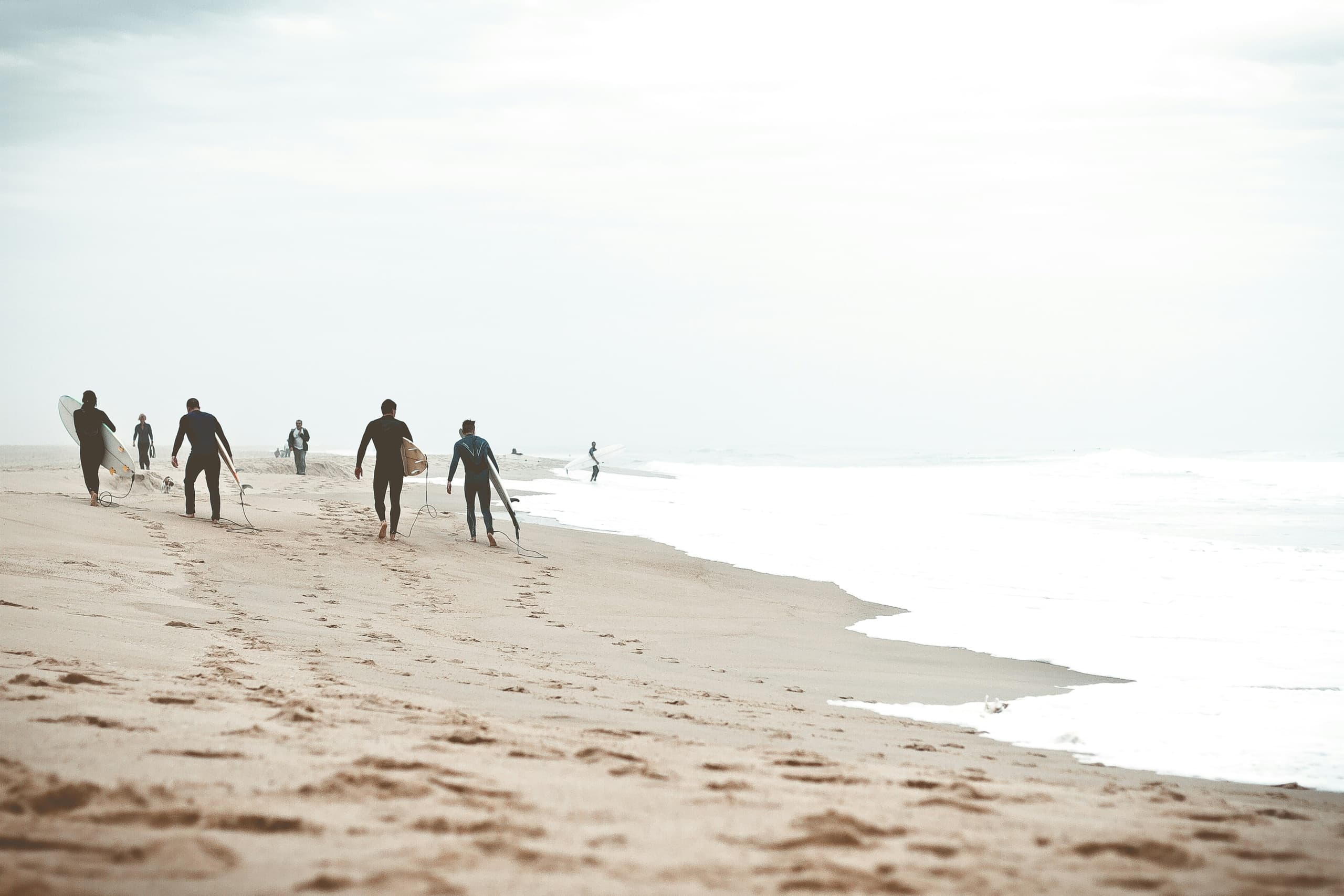 Surfers walking along misty sandy beach at low tide