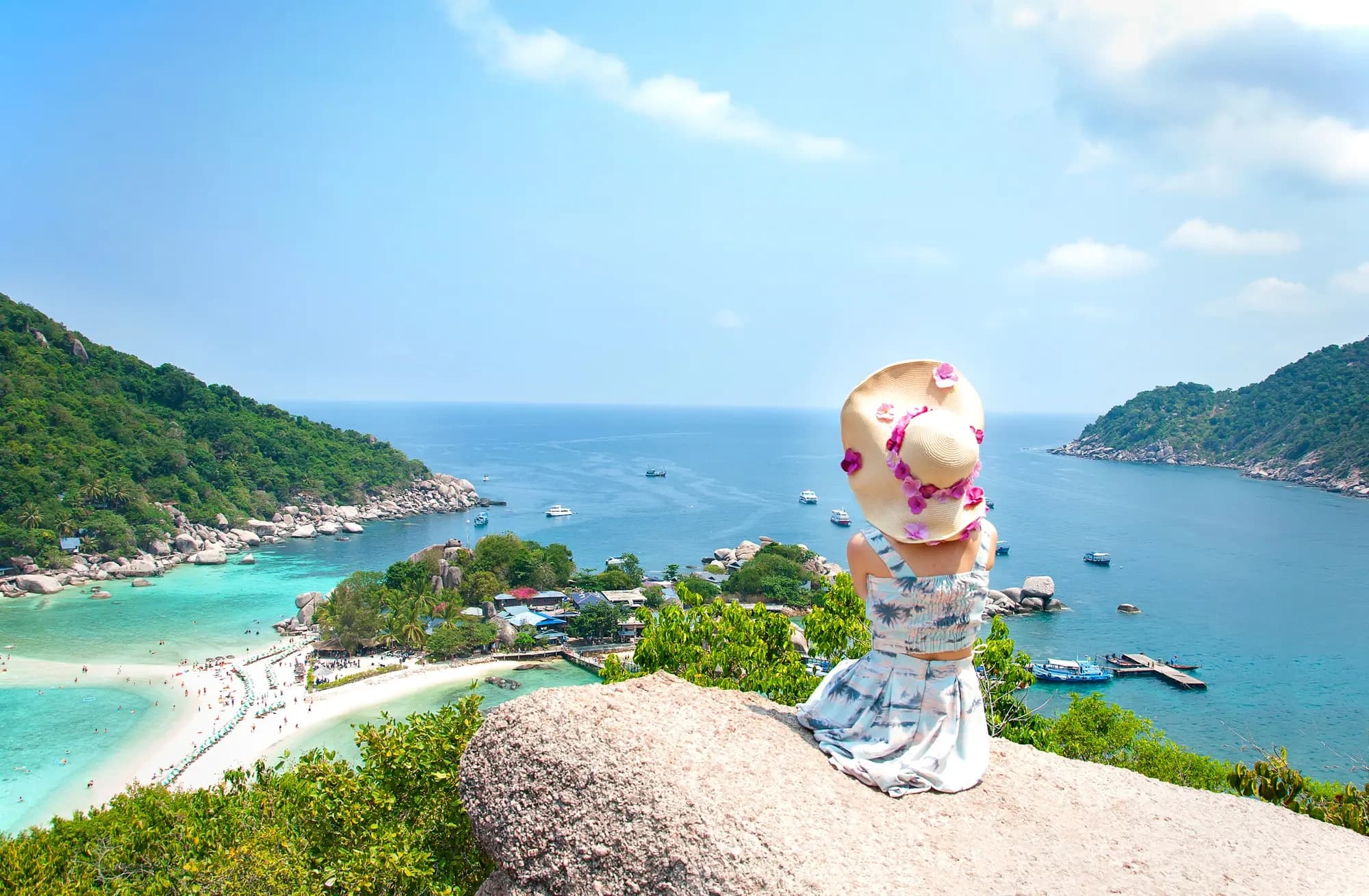 Traveler sitting on cliff overlooking turquoise island bay, panoramic view