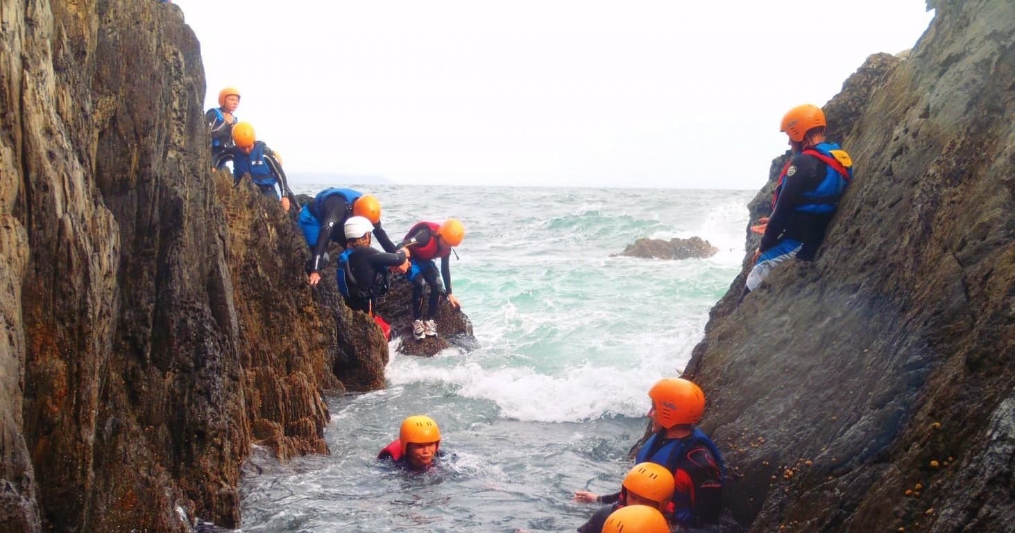 Coasteering group navigating narrow rocky coastal inlet