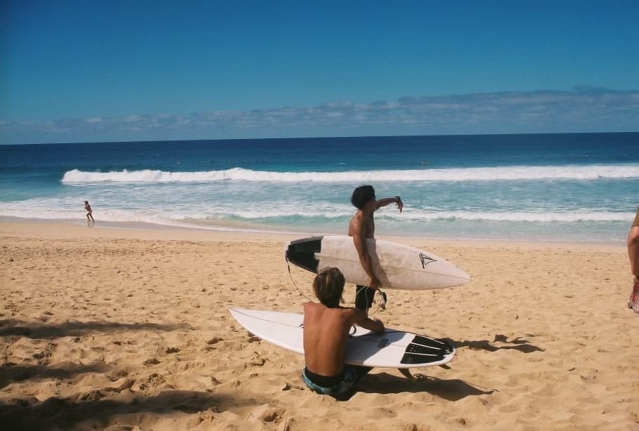 Surfers carrying boards and relaxing on a sandy ocean beach