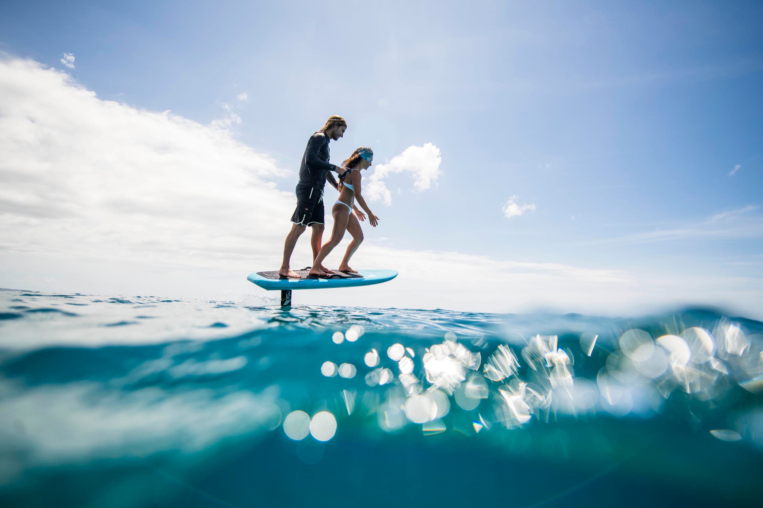 E-foil riders gliding above clear ocean waves, scenic coastal ride