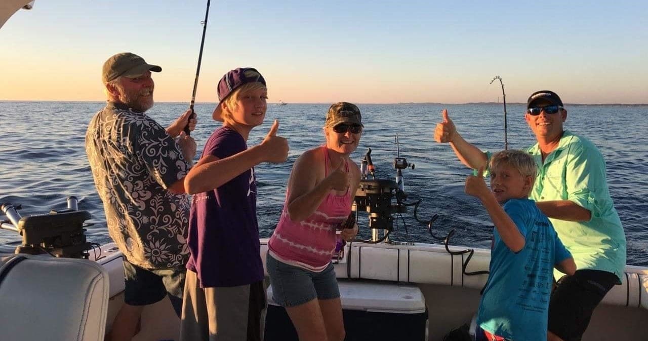 Family anglers celebrating catch on charter boat at sunset