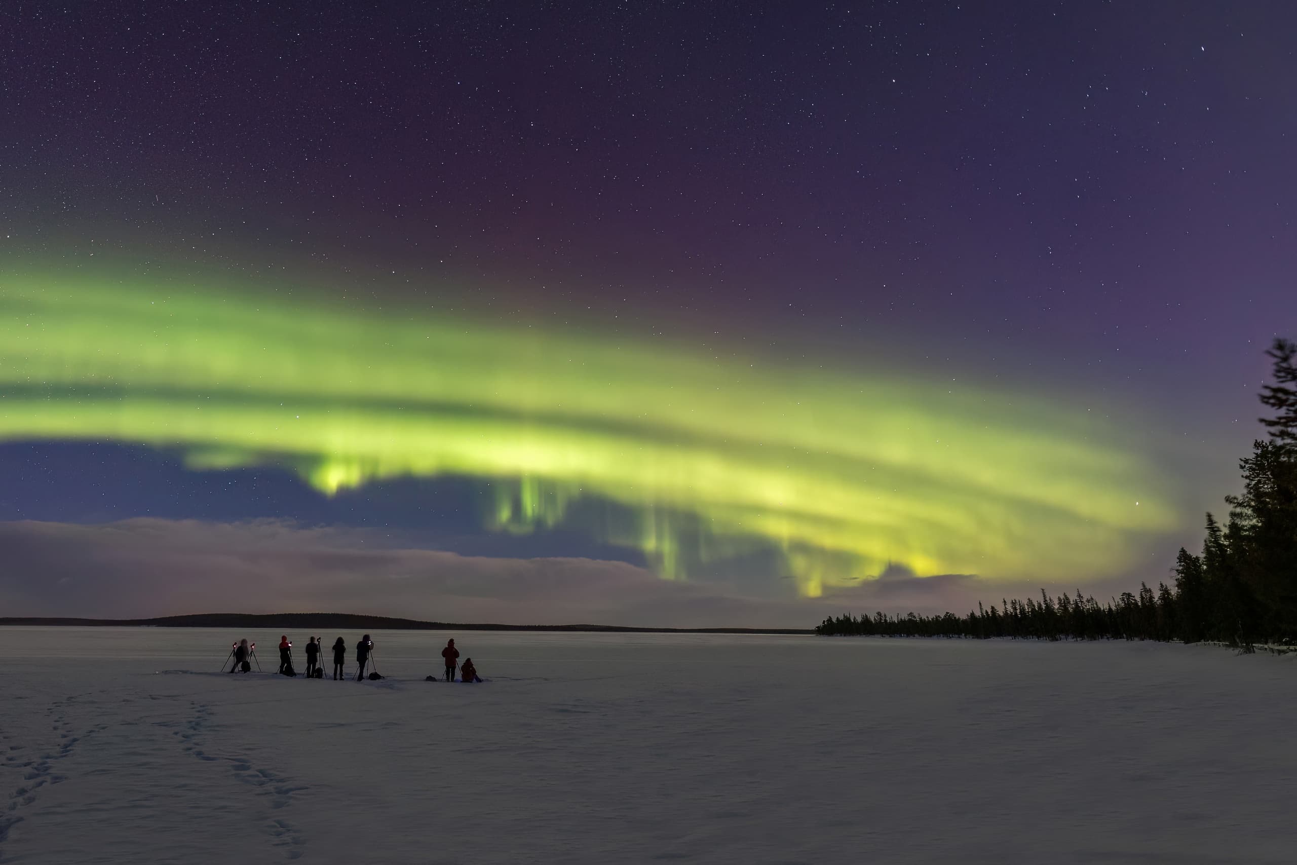 Aurora borealis above frozen lake with silhouetted observers
