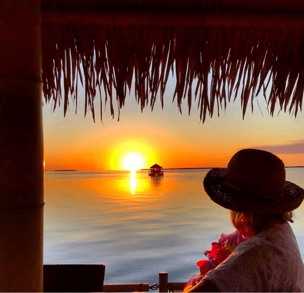 Person watching sunset from tiki hut over calm Miami bay waters